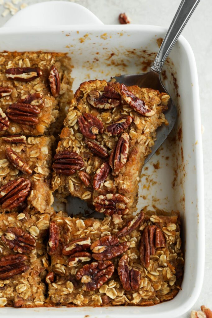 Sweet Potato Pie Baked Oatmeal served in casserole dish with pie server with pecans and oats 