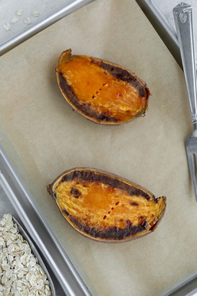 baked sweet potato on parchment lined baking sheet with fork and oats