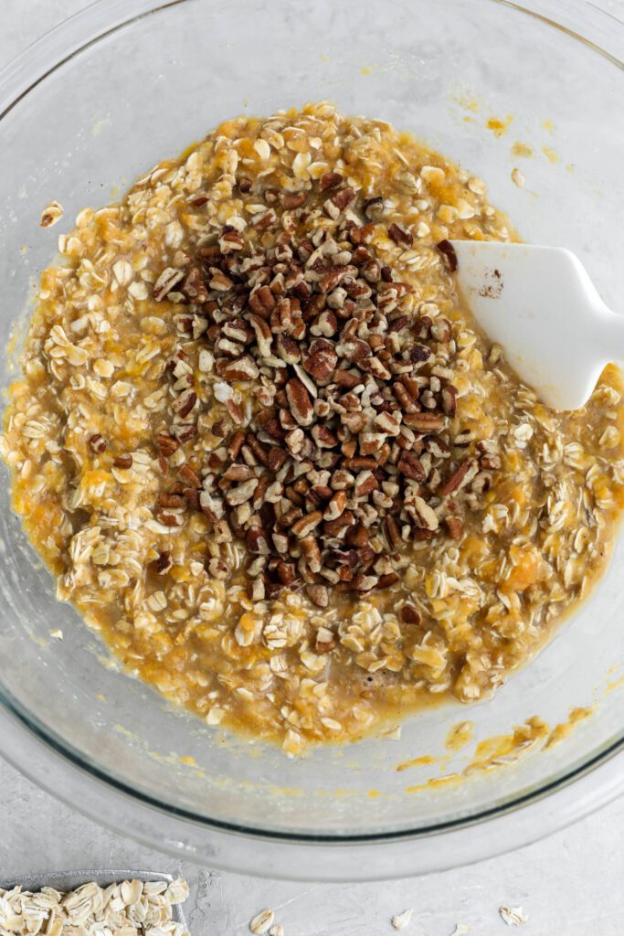 sweet potato pie baked oats batter in bowl topped with pecans with spatula