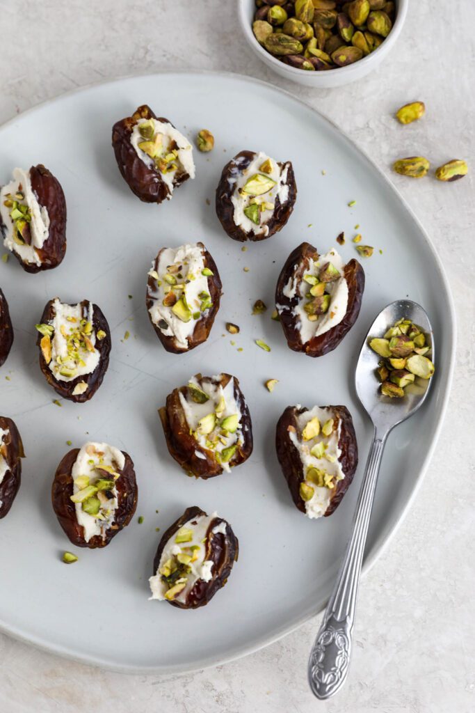 Dates stuffed with cream cheese and topped with pistachios on white plate
