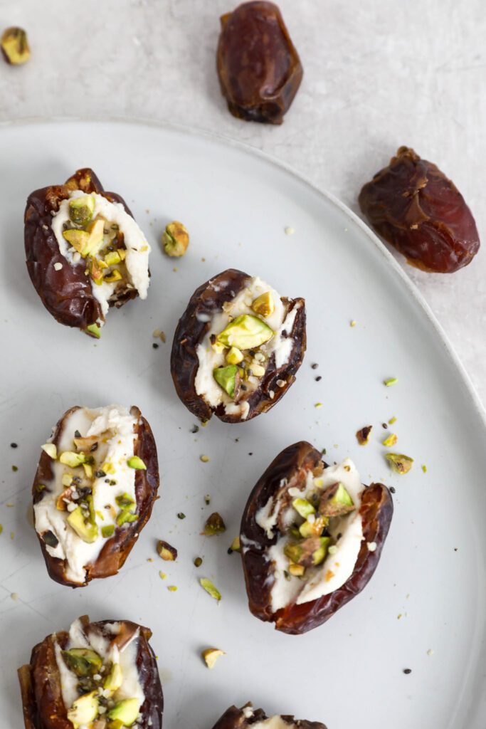 Dates stuffed with cream cheese and topped with pistachios, hemp hearts, and chia seeds on white plate