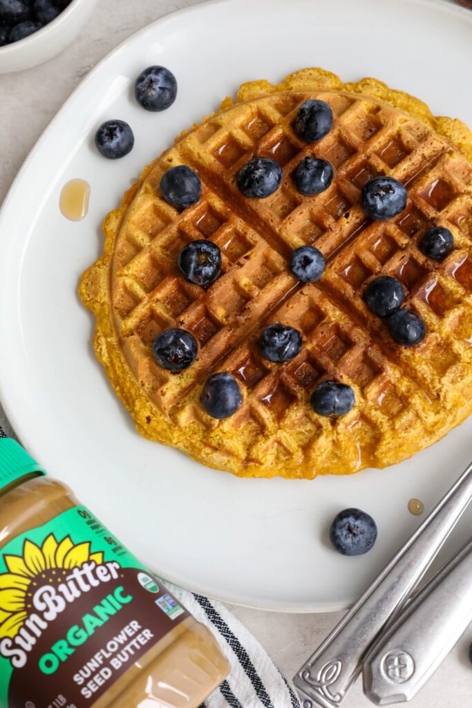 Sweet Potato Waffles served on a plate topped with maple syrup and blueberries with SunButter jar
