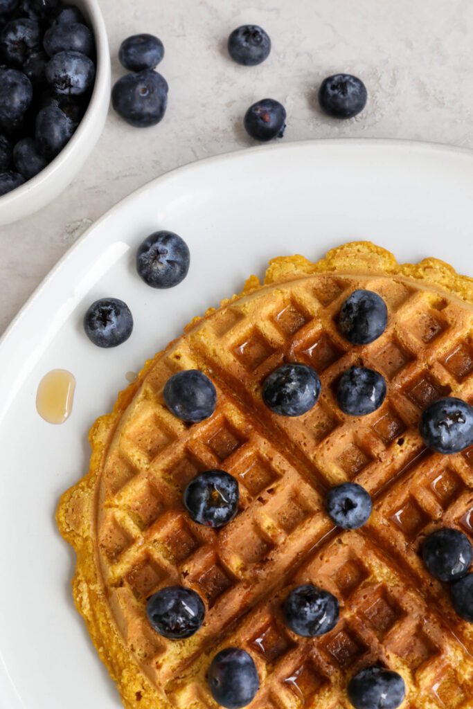 Sweet Potato Waffles served on a plate topped with maple syrup and blueberries 