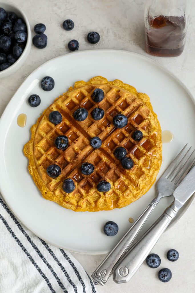 Sweet Potato Waffles served on a plate topped with maple syrup and blueberries with a fork and knife