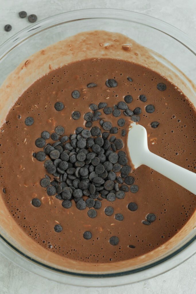 Red Velvet Baked Oats Batter in mixing bowl with spatula topped with dark chocolate chips 