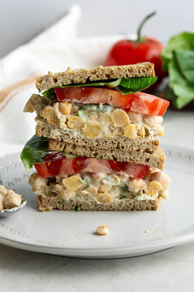 Vegan Chickpea Salad Sandwich stacked on plate with lettuce and tomato in background