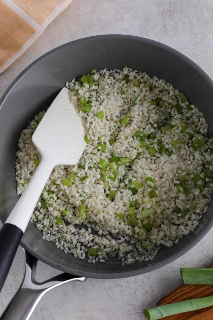 arborio rice with cooked green onion and spatula in saucepot
