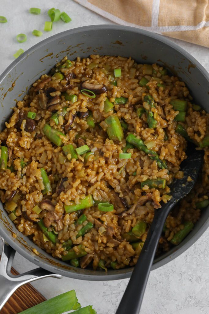 Mushroom & Asparagus Risotto cooked in pan with spatula topped with green onion