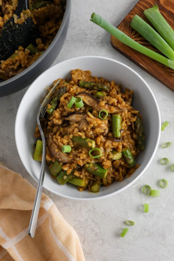 Mushroom & Asparagus Risotto served in a bowl topped with green onion with a fork and towel