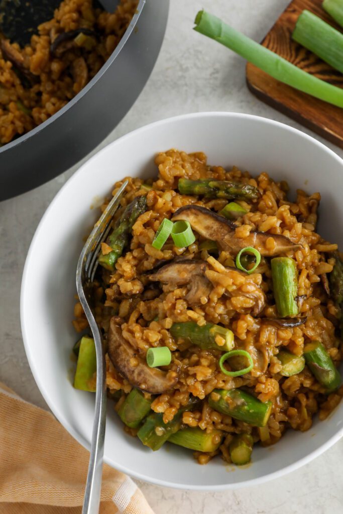 Mushroom & Asparagus Risotto served in a bowl topped with green onion with a fork and towel