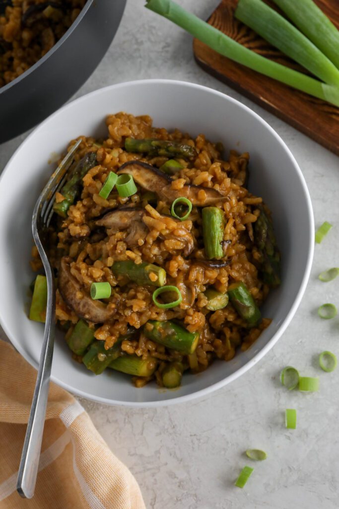 Mushroom & Asparagus Risotto served in a bowl topped with green onion with a fork and towel