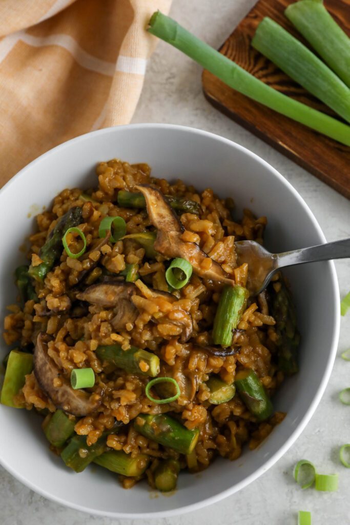 Mushroom & Asparagus Risotto served in a bowl topped with green onion with a fork and towel
