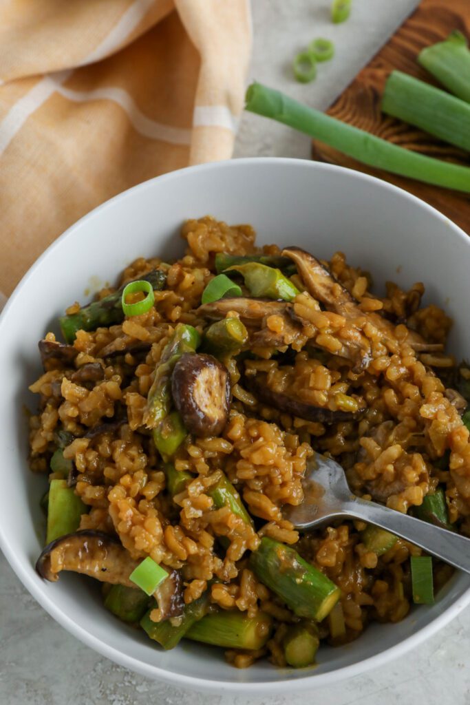 Mushroom & Asparagus Risotto served in a bowl topped with green onion with a fork and towel