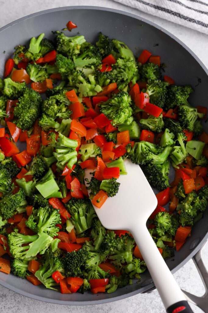 broccoli and red bell pepper sautéed in pan with spatula 
