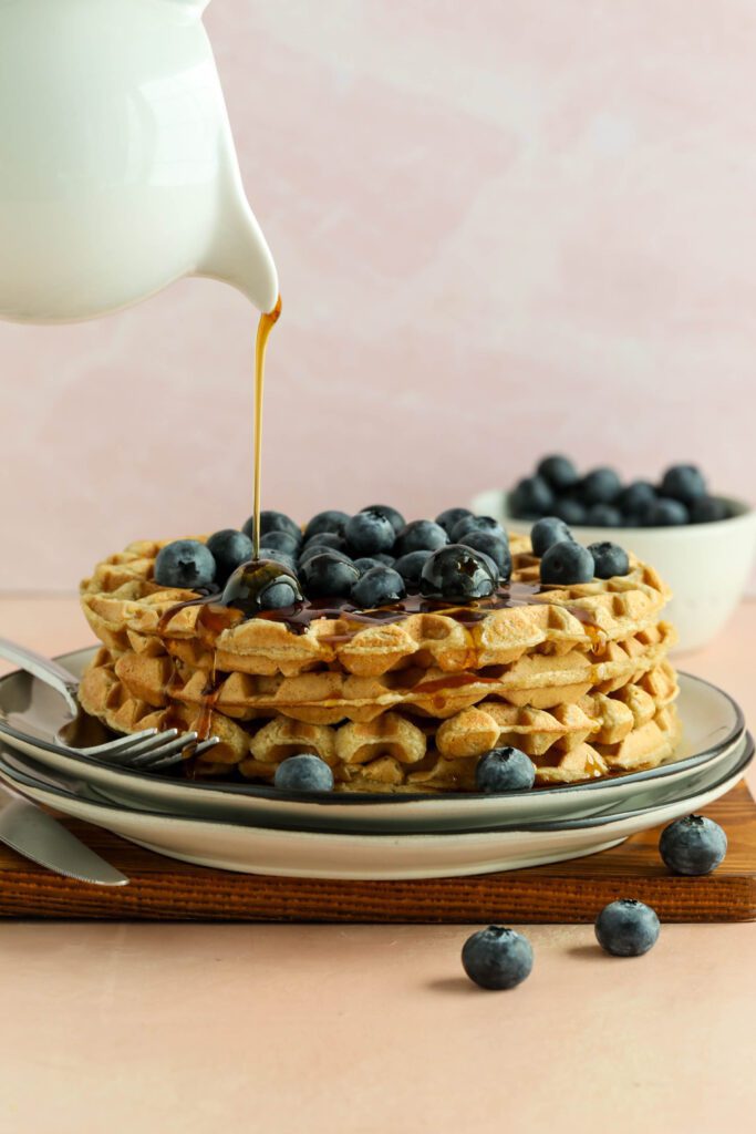 Vegan Applesauce Waffles stacked on plate with blueberries drizzled with maple syrup