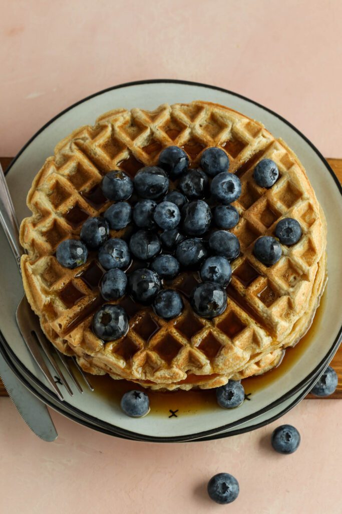 Vegan Applesauce Waffles stacked on plate with blueberries drizzled with maple syrup