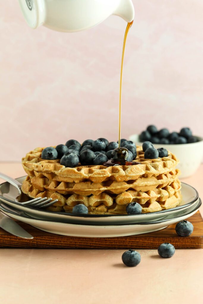 Vegan Applesauce Waffles stacked on plate with blueberries drizzled with maple syrup
