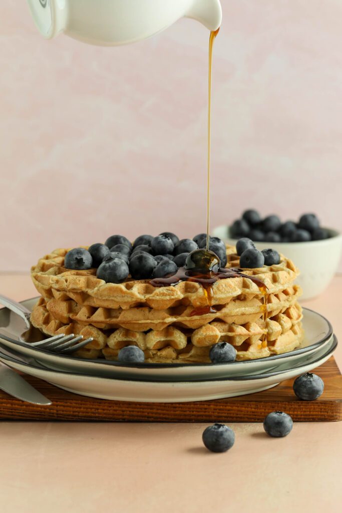 Vegan Applesauce Waffles stacked on plate with blueberries drizzled with maple syrup