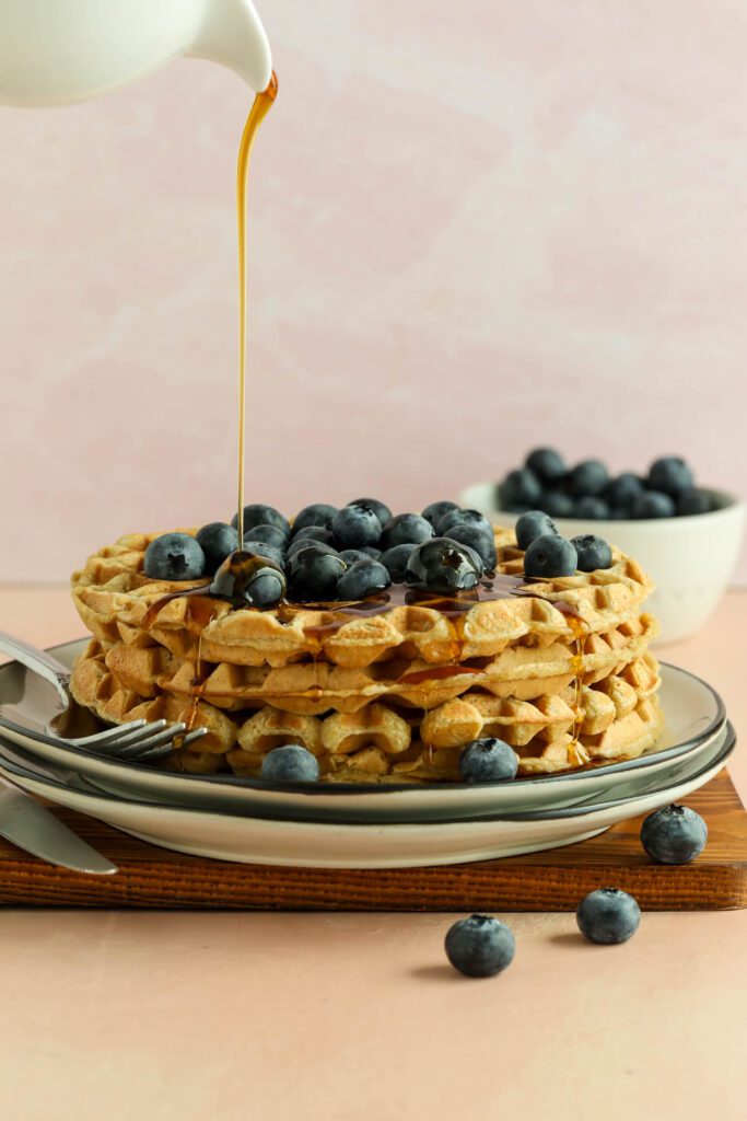 Vegan Applesauce Waffles stacked on plate topped with blueberries and maple syrup