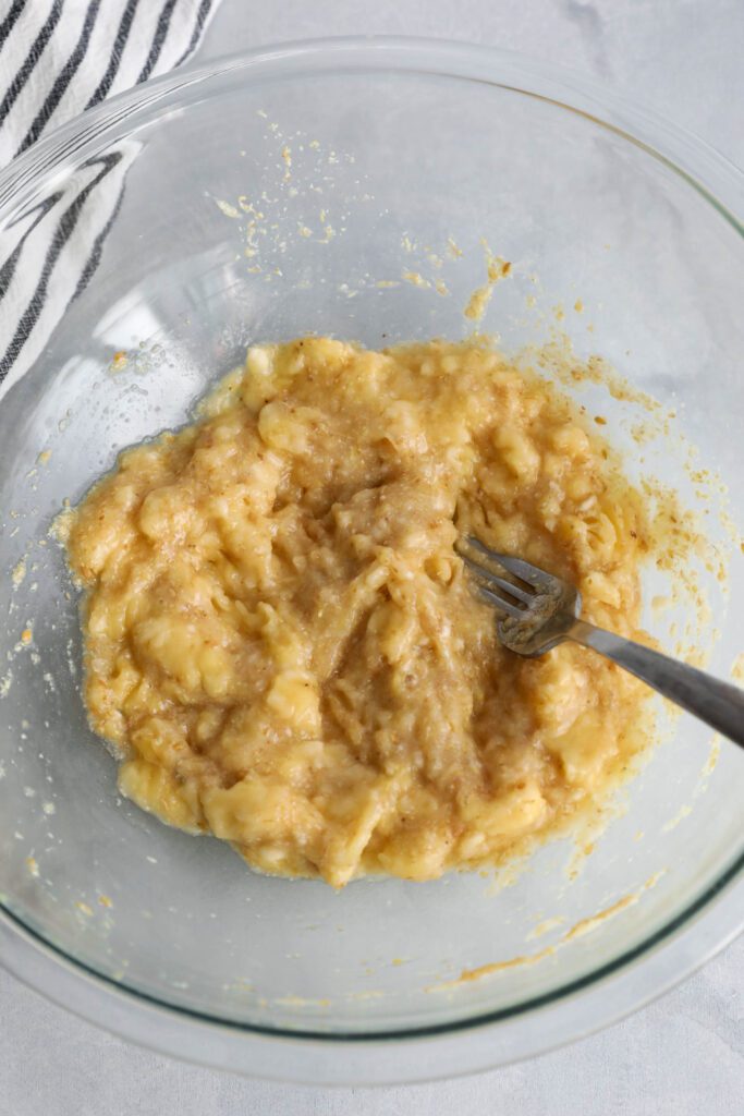 smashed banana in large mixing bowl with fork