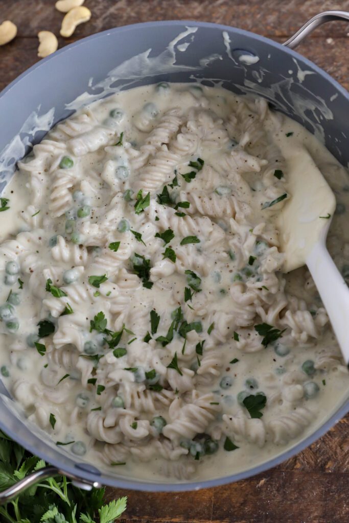 Cauliflower Cashew Alfredo in pot with spatula topped with parsley and pepper