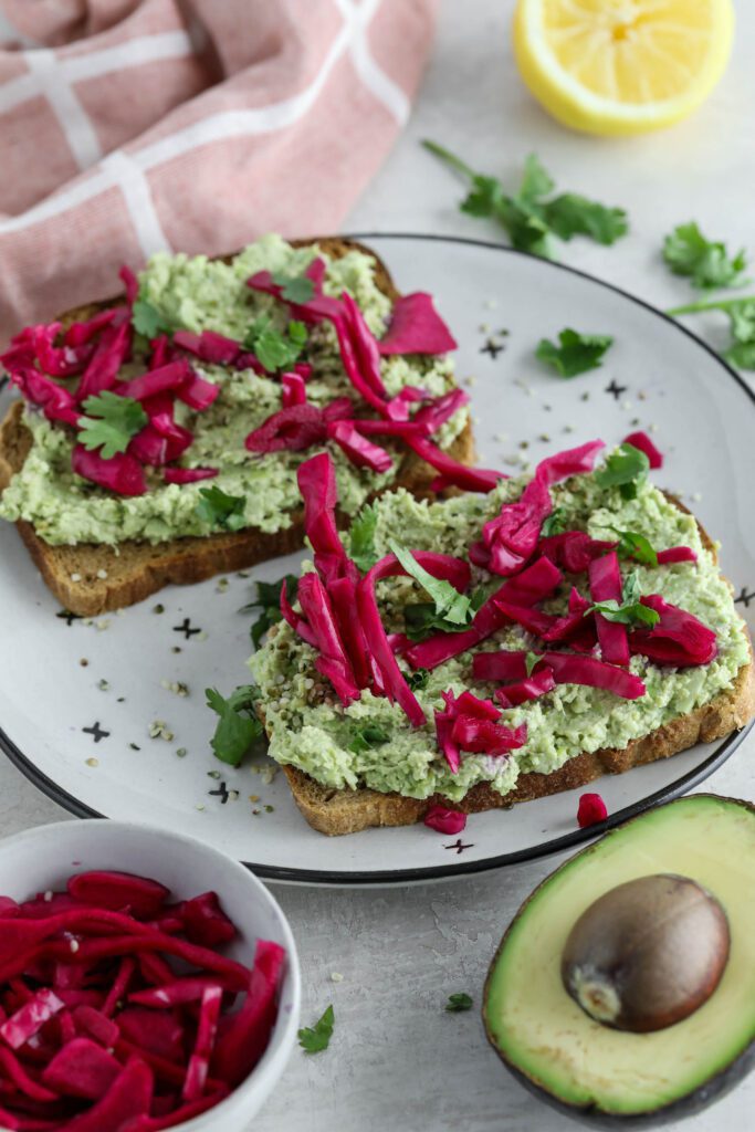 Smashed Edamame Toast served on plate topped with pickled cabbage and cilantro with pink towel