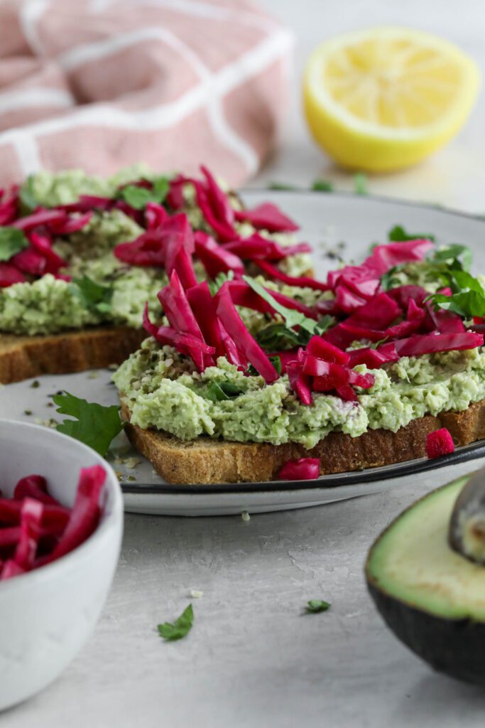 Smashed Edamame Toast served on plate topped with pickled cabbage and cilantro with pink towel