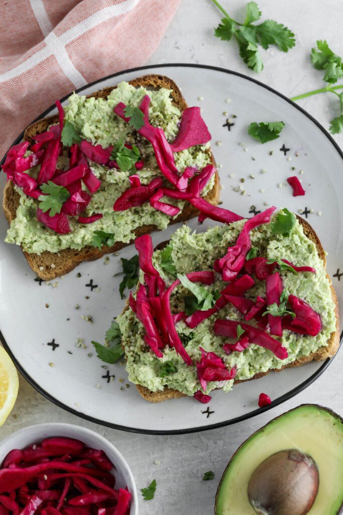 Smashed Edamame Toast served on plate topped with pickled cabbage and cilantro with pink towel