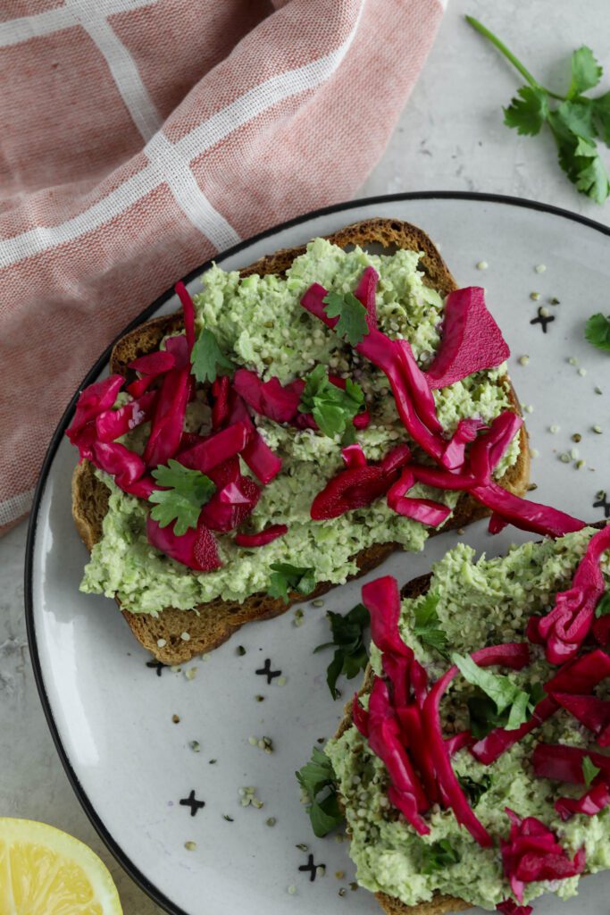 Smashed Edamame Toast served on plate topped with pickled cabbage and cilantro with pink towel