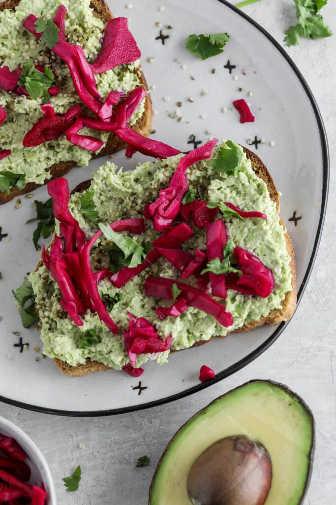 Smashed Edamame Toast served on plate topped with pickled cabbage and cilantro with pink towel