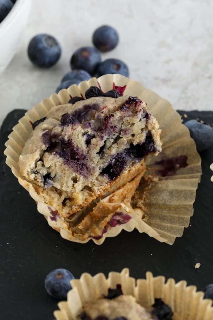 Vegan Blueberry Muffins served on black rectangle with glass of milk, knife, and blueberries 