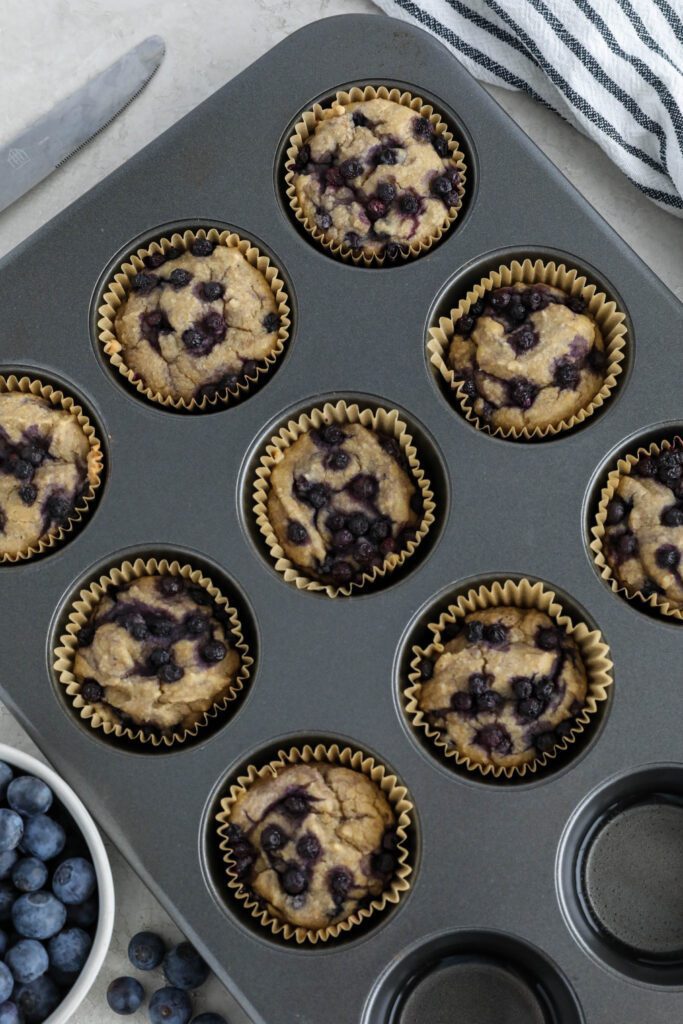 Vegan Blueberry Muffins baked in muffin tin with fresh blueberries and knife on side