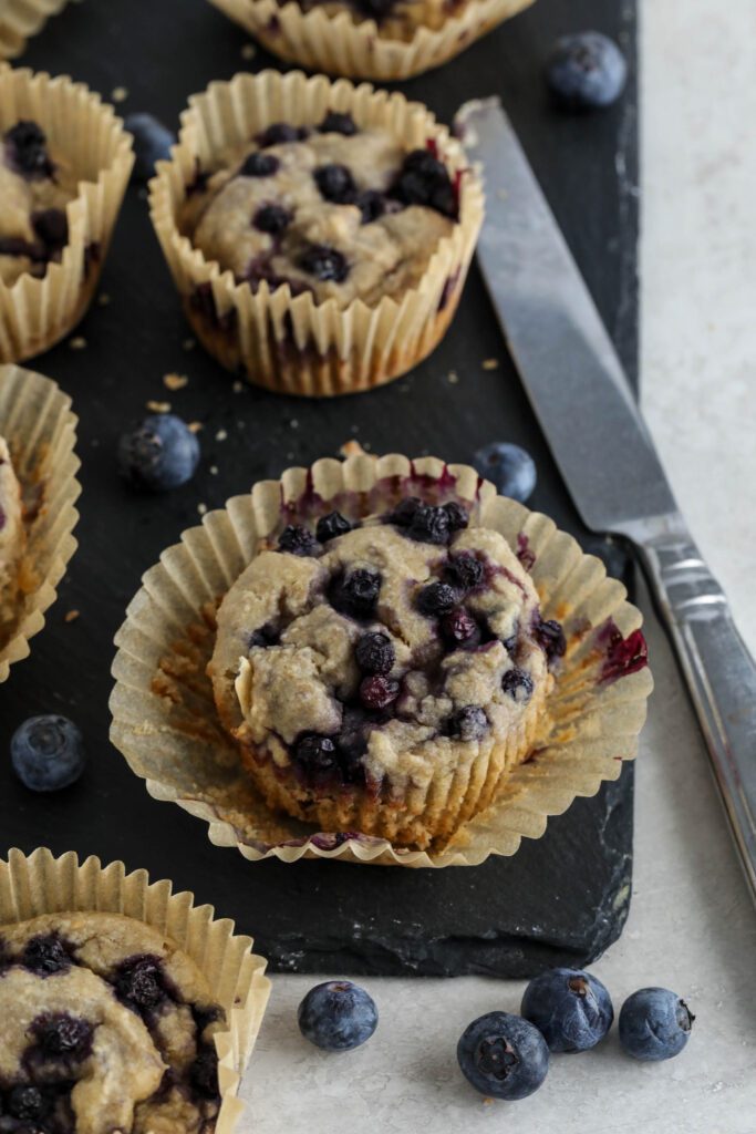 Vegan Blueberry Muffins served on black rectangle with glass of milk, knife, and blueberries 