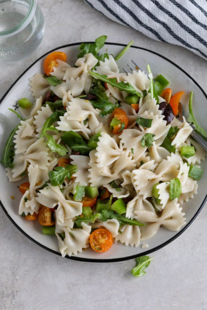 Easy Vegan Pasta Salad served on plate with fork and glass of water with blue and white striped towel 