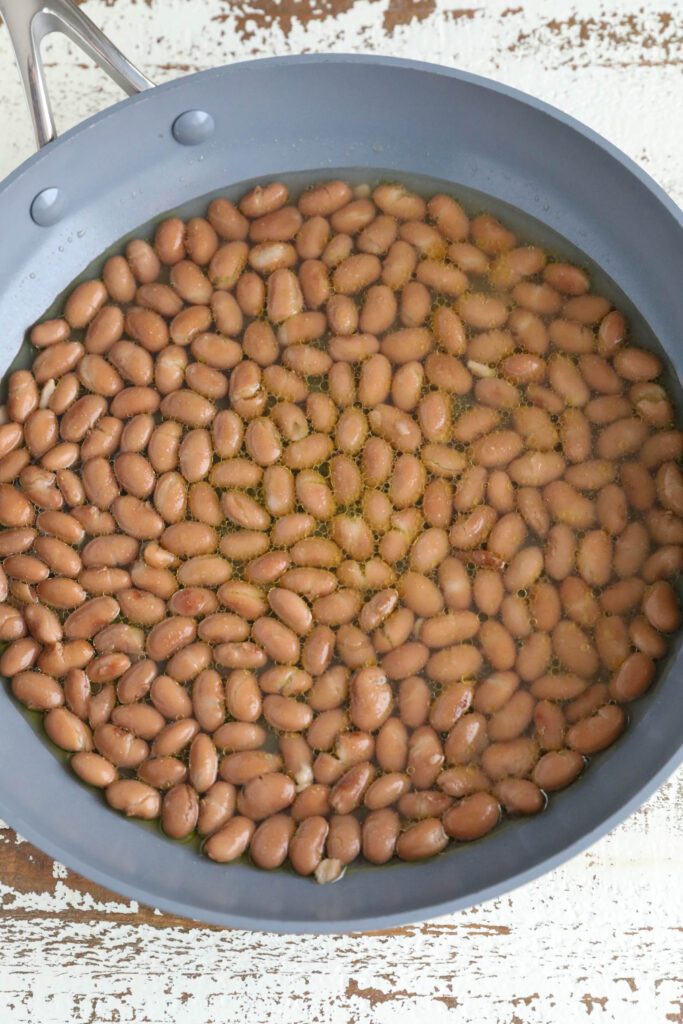 pinto beans with oil and water and seasoning in green pan 