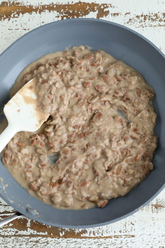 refried pinto beans in green pan with spatula 