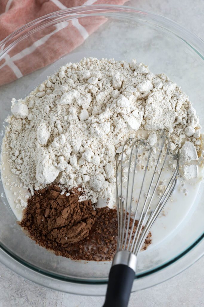 ingredients for vegan chocolate waffle batter in bowl with whisker 