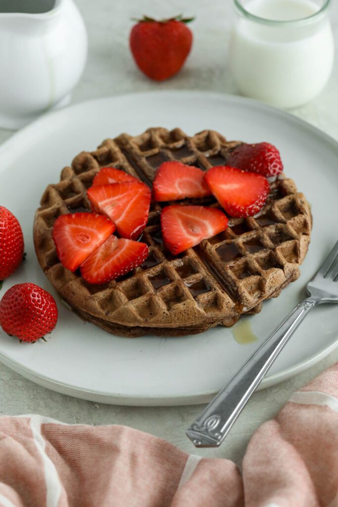 Vegan Chocolate Waffles served on white plate topped with strawberries and maple syrup