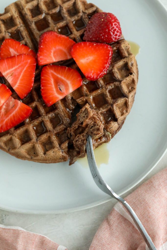 Vegan Chocolate Waffles served on white plate topped with strawberries and maple syrup