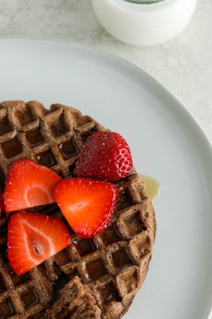 Vegan Chocolate Waffles served on white plate topped with strawberries and maple syrup