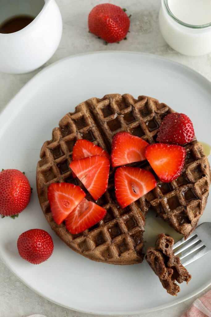 Vegan Chocolate Waffles served on white plate topped with strawberries and maple syrup