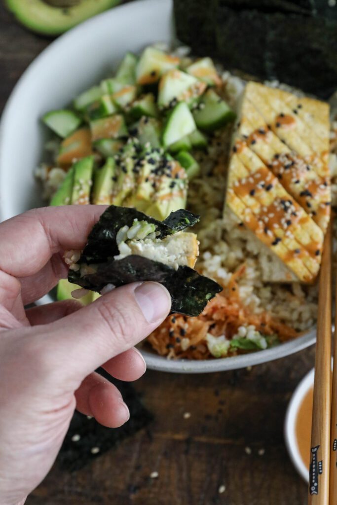 Vegan Viral "Salmon" Bowl served in a bowl with chopsticks and black and white sesame seeds with hand picking up nori