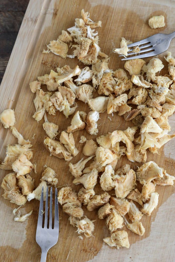 rehydrated lion's mane mushrooms torn with forks on wooden board