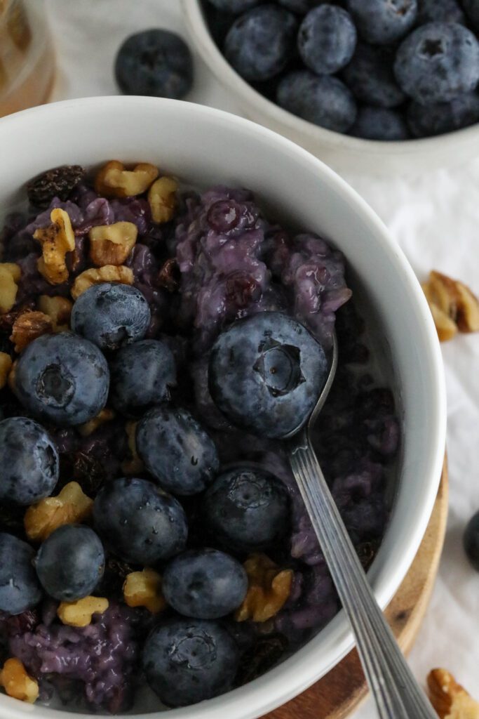 Blueberry Stovetop Oatmeal served on wooden pedestal with scattered blueberries and walnuts with spoon 