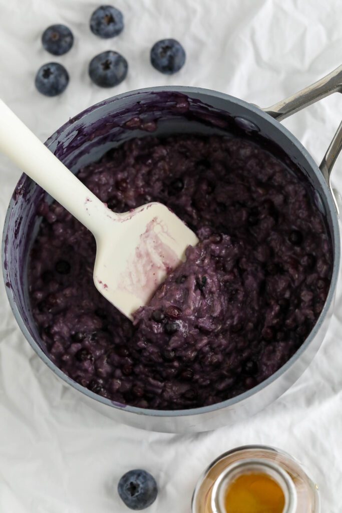 Blueberry Stovetop Oatmeal cooked in pot with spatula and blueberries on the side 