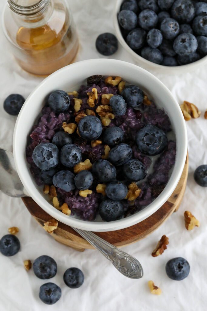 Blueberry Stovetop Oatmeal served on wooden pedestal with scattered blueberries and walnuts with spoon 