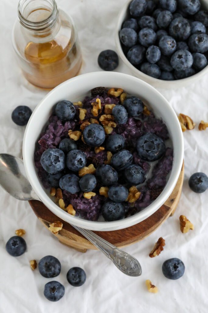 Blueberry Stovetop Oatmeal served on wooden pedestal with scattered blueberries and walnuts with spoon 