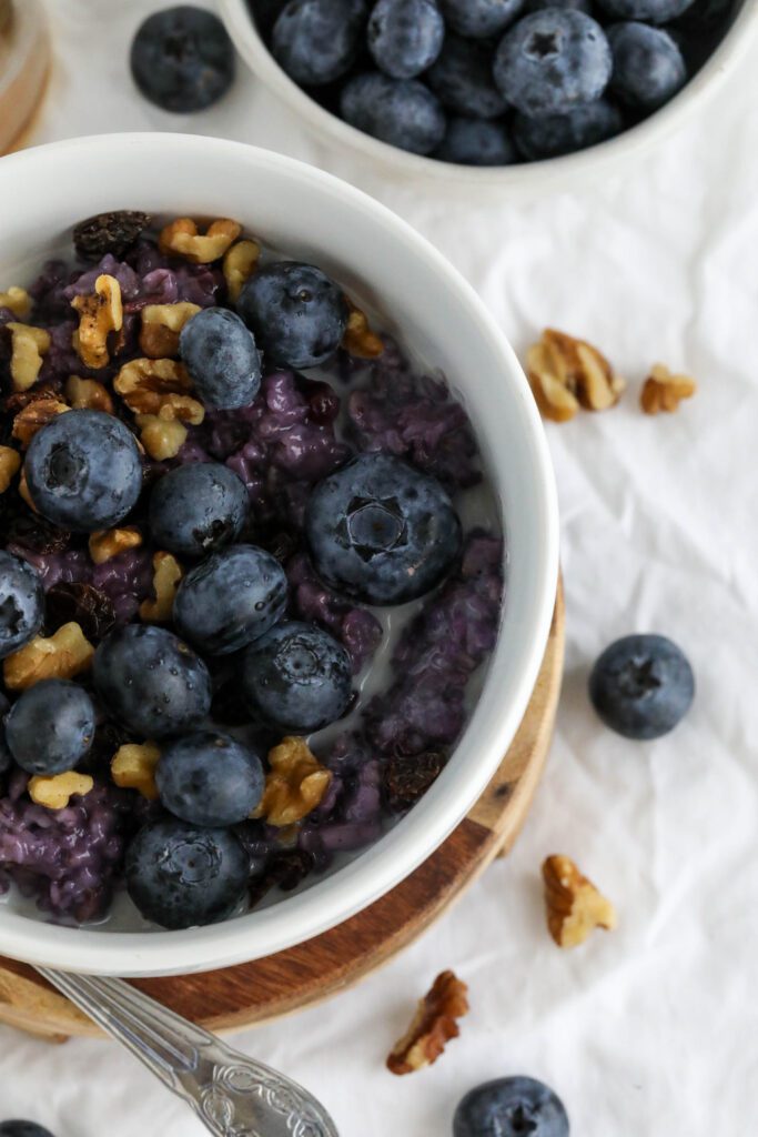 Blueberry Stovetop Oatmeal served on wooden pedestal with scattered blueberries and walnuts with spoon 