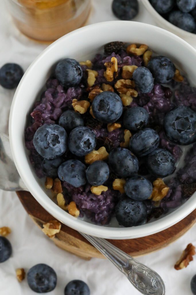 Blueberry Stovetop Oatmeal served on wooden pedestal with scattered blueberries and walnuts with spoon 