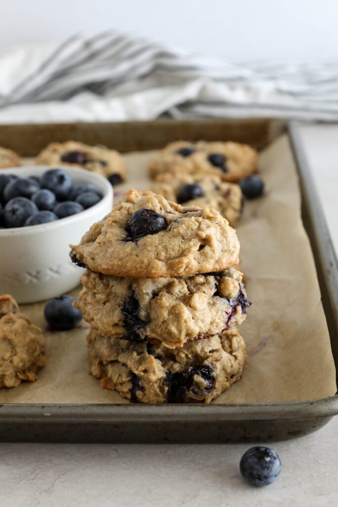 Blueberry SunButter Breakfast Cookies stacked on parchment lined baking sheet with blueberries scattered